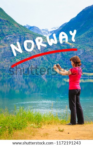 Tourism and travel. Woman tourist taking photo with camera, enjoying mountains lake Oppstrynsvatnet view in Jostedalsbreen National Park, Oppstryn (Stryn), Sogn og Fjordane county. Norway Scandinavia.