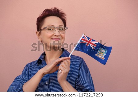Falkland Islands flag. Woman holding Falkland Islands flag. Nice portrait of middle aged lady 40 50 years old with a national flag over pink wall on the street outdoors.
