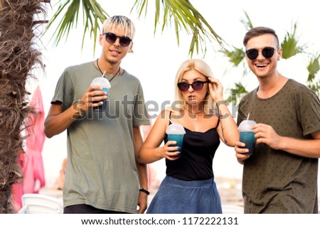 three friends cheerful company rest on a tropical beach and drink cocktails, very, magazine concept