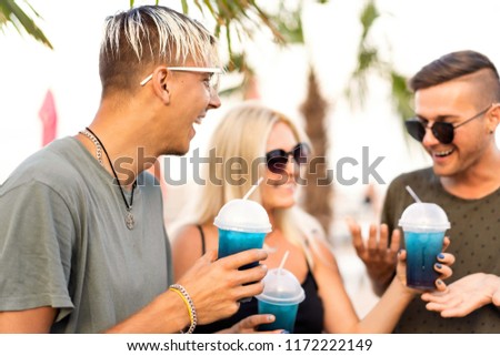 three friends cheerful company rest on a tropical beach and drink cocktails, very, magazine concept