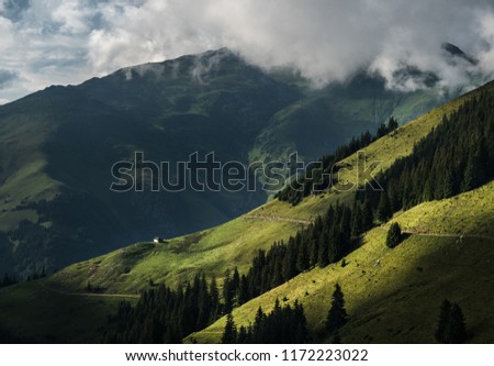 Panoramic view of an isolated chalet in the mountains. Isolated chalet in the mountains under a misty peak. Green mountain fields, travel hike road and mountain forest view. Royalty-Free Stock Photo #1172223022