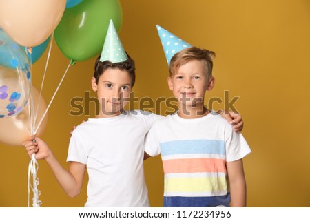 Cute little boys in Birthday hats and with balloons on color background