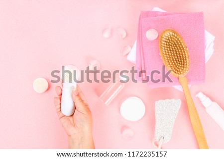 Bathroom accessories on a pastel pink background. Top view, copy space. Face cleansing brush in hand.