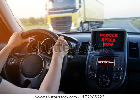 the girl driving rushes on the route, an inscription on the monitors "reduce speed now" and "attention".