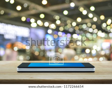 Camera flat icon on modern smart mobile phone screen on wooden table over blur light and shadow of mall, Business camera online shopping and service concept