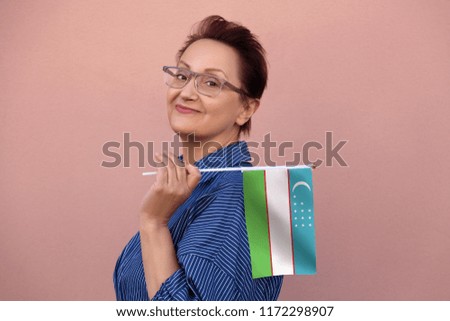Uzbekistan flag. Woman holding Uzbekistan flag. Nice portrait of middle aged lady 40 50 years old with a national flag over pink wall background outdoors.