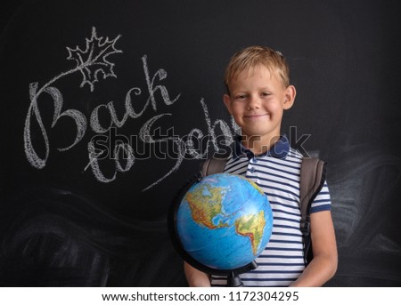 European boy with physical globe on black school Board background with English inscription back to school