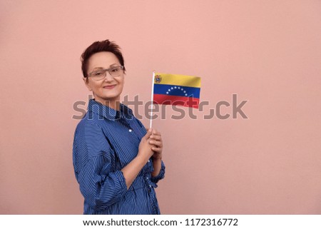 Venezuela flag. Woman holding Venezuela flag. Nice portrait of middle aged lady 40 50 years old with a national flag over pink wall background outdoors.