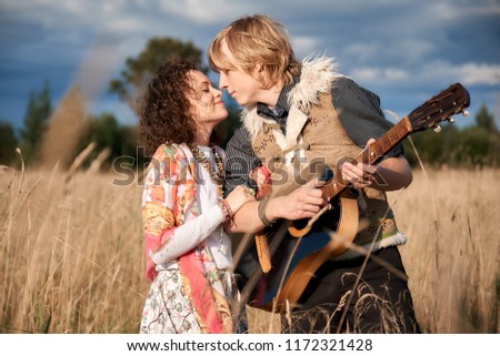 Boho style attractive couple in love posing on the autumn field. Family having fun and laughing, play guitar.  Gypsy style clothes. Young blonde man and beautiful caucasian woman together outdoor.