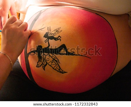 Female artist painting the belly of a pregnant young woman with body paints and brushes Royalty-Free Stock Photo #1172332843