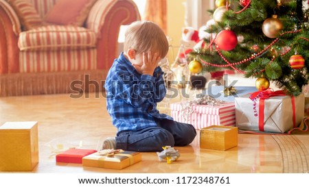Little boy sitting under Christmas tree and crying