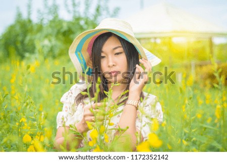 A woman portrait wearing a flower dress with broad brim hat and stand in the yellow flower field of Sunn Hemp (Crotalaria Juncea)