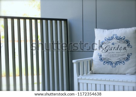 Wooden bench and a pillow with sign “Garden” in English letters and the way to pronounce the word “Garden”  in English printed on the pillow.