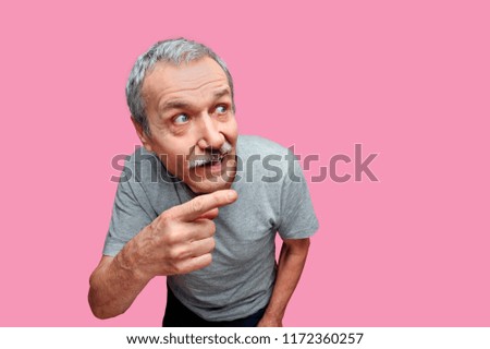 Funny senior man against pink background pinting to the copy space area