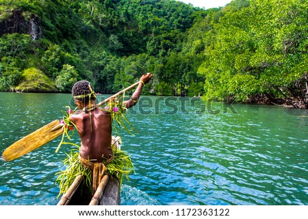 Yang sportive indigenous tribal boy with a paddle in a traditional canoe, natural green jungle with mangrove trees background, Melanesia, Papua New Guinea, Tufi Royalty-Free Stock Photo #1172363122