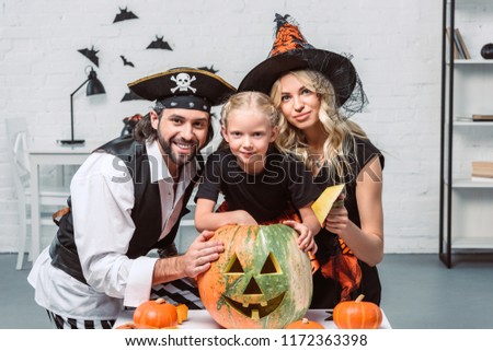 portrait of parents and little daughter in halloween costumes at table with pumpkins at home