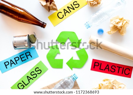 Matherials suitable for recycle near green recycle eco symbol. Words paper, glass, plastic, cans on white background top view