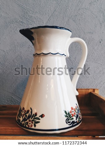 White handmade ceramic vase with flower ornament at wooden shelve at grey background