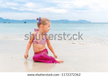 Little beautiful girl dressed in swimsuit as a mermaid sits on the seashore
