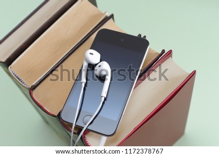 Phone with white earpods on stack of books audiobook storytel podcast music concept