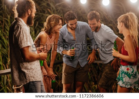 Group of young men and women laughing at at outdoor summer party.