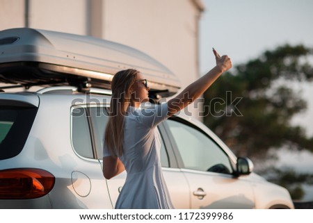 Beautiful young woman taking self portraits with smartphone, at sunset,  in car background. top view.