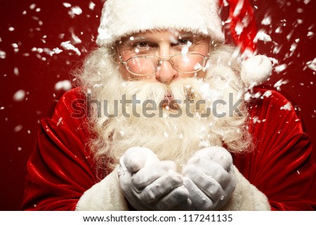 Photo of Santa Claus in eyeglasses blowing snow and looking at camera