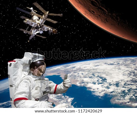 Astronaut shows the thumbs-up about flying to Mars. Space station on the backdrop. The elements of this image furnished by NASA.

