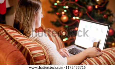 Closeup photo of beautiful young woman relaxing in armchair next to Christmas tree and making online purchases