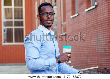 stylish and young African student American man holding glass with coffee in summer in park red brick building background