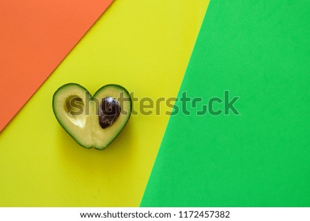 Heart-shaped slices of avocado on green, orange, yellow background