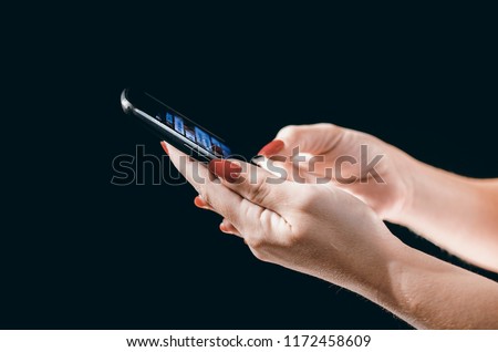 Young woman's hands  with red painted fingernails holding a cell phone or mobile on black background.