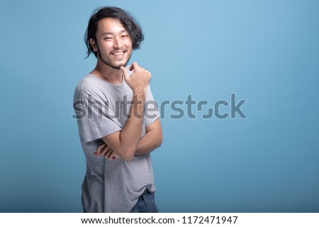 Young bearded man confident finger touching chin portrait in blue background. Asian young hipster standing finger touching jaws, confident smile, half body shot. Young generation hipster concept. Royalty-Free Stock Photo #1172471947