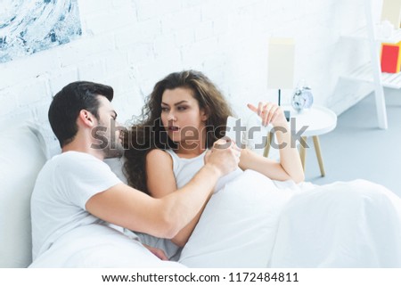 young couple holding smartphone and quarreling in bed, relationship difficulties concept