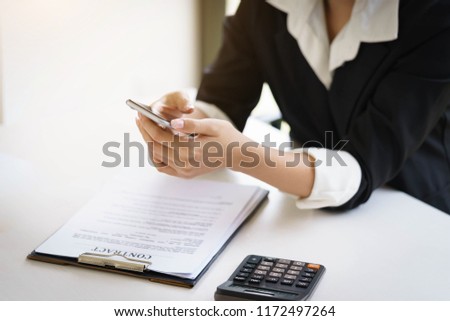 Businesswoman working with a mobile phone above the contract and calculator  while sitting at the wooden table. Royalty-Free Stock Photo #1172497264