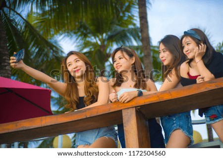 lifestyle portrait of group with young happy and attractive Asian Chinese and Korean women hanging out , girlfriends enjoying holidays trip in tropical resort taking selfie picture with mobile phone 