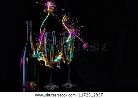 Glasses and a bottle of champagne in the light of Bengal lights. Black background. The concept of the celebration of the wedding and the new year. Copy space.