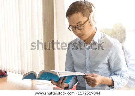 At library,man open and read book,listen music by ear phone,Education background.