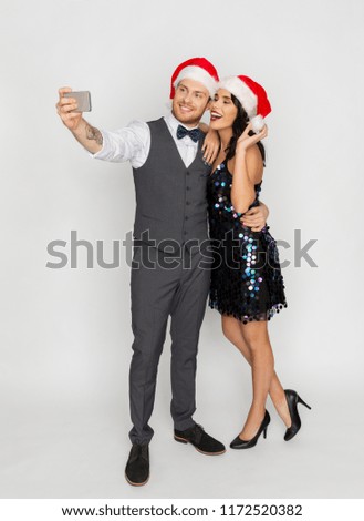 celebration, people and holidays concept - happy couple in santa hats taking selfie by smartphone at christmas or new year party