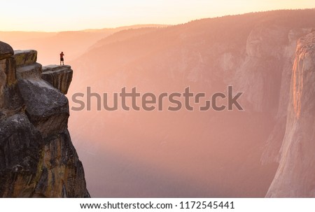 A hiker stands at the edge of a cliff at Taft Point overlooking El Capitan in Yosemite National Park, California. Royalty-Free Stock Photo #1172545441