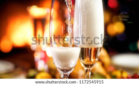 Closeup photo of champagne flowing in glasses on romantic dinner at fireplace