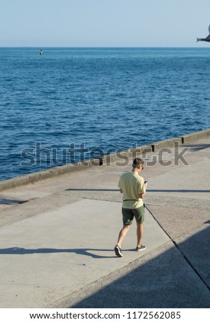 Modern fashionable young man walking alone on the sea promenade, looking at your gadget