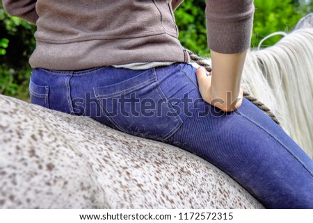 Young pretty girl riding a horse without saddle. Detail picture of back of horse, blue jeans and woman's hands. 