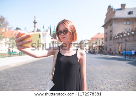 Attractive girl tourist on background takes selfie streets of the old town. Walking along the old city on a sunny summer day. Tourist girl takes selfie on the streets of Prague, Czech Republic