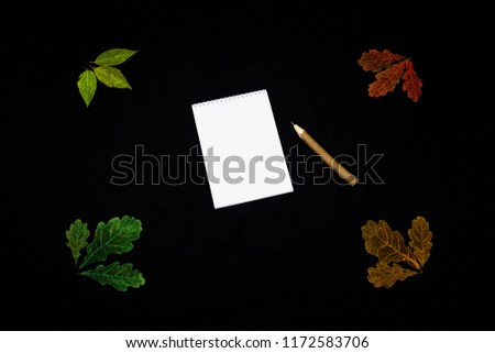 Pencil on a blank notebook, around there are bright leaves