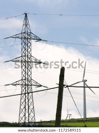 Vertical view of three different types of energy, old electric post, modern electric post and wind turbine in summer green landscape.