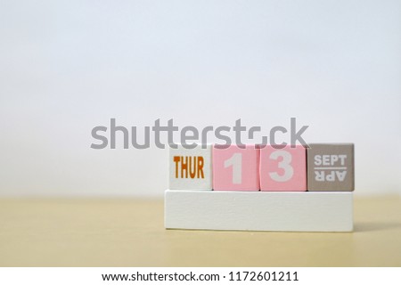 Thursday 13th September, Soft selective focus on pink wooden block calendar on burred wooden table with white cement background, copy space for text or wording.