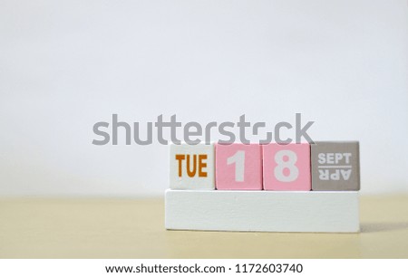 Tuesday 18th September, Soft selective focus on pink wooden block calendar on burred wooden table with white cement background, copy space for text or wording.