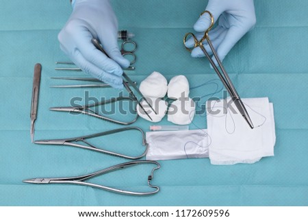 Doctor's hand holding scalpel and vascular clamps in the operating room. Instruments for surgery arranged on blue background top view. Medical and surgery concept. Medical and surgery concept.