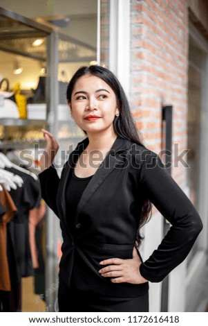 The cute woman wearing black uniform is acting to be taken photo during her working in the plaza or office with the brick background style.
